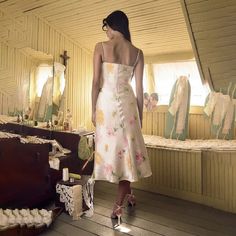 a woman in a dress standing on a wooden floor next to an old trunk and mirror