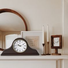 a clock sitting on top of a mantle next to two candles and a framed photograph