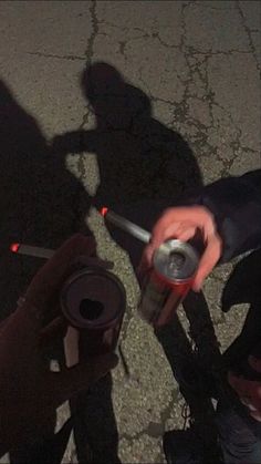 two people standing next to each other holding cans and drinking from them with their shadows on the ground