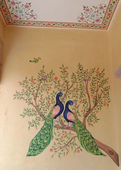 two peacocks sitting on top of a tree in a room with painted ceiling tiles