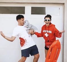 two people in red shirts and black shorts holding an orange life preserver while standing next to a white garage door