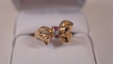 "For your consideration is a lovely 14K yellow gold ring with one genuine natural diamond accent stone and a couple of genuine ruby accents stones in a ribbon tie design. The ring weights 5.41 grams. It is in U.S. size 6-6.25. It is hallmarked \"14K\". The diamond was tested as genuine. The center one is approximately 1.9 mm in diameter. The ribbon is approximately 22 x 12 mm at the widest. It is a lovely ring and a perfect gift. Great vintage condition. Photos are part of description. The case Yellow Gold Cocktail Ring, Ribbon Ring, Gold Cocktail Ring, Gold Cocktail, Tie Design, Ribbon Design, Lovely Ring, Genuine Turquoise, Yellow Gold Ring