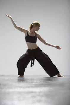 a woman standing on one leg with her arms out in the air while wearing black pants