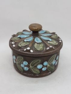 a decorative box with blue flowers and leaves painted on the front, sitting on a white surface