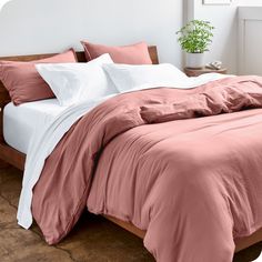 a bed with pink sheets and pillows in a white room next to a potted plant