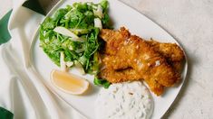 a white plate topped with fried chicken next to a salad