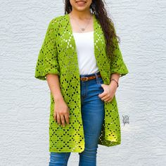 a woman standing in front of a white wall wearing a green crochet cardigan