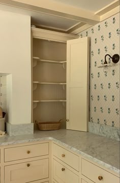 an empty kitchen with white cabinets and marble counter tops in front of a wallpapered wall