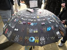 an umbrella is covered with earrings and earring hooks as people walk by in the background