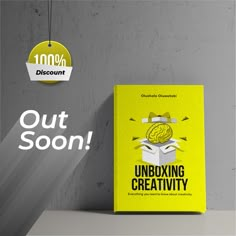 a yellow book sitting on top of a table next to a gray wall with the words, out soon unboxing creativity