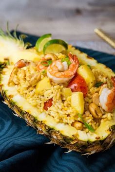 a pineapple filled with rice and shrimp next to a fork on a blue towel