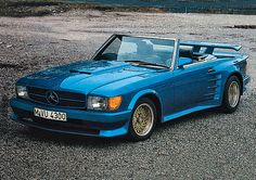 a blue convertible car parked on top of a gravel road