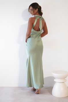 a woman in a long green dress standing next to a white vase and looking at the wall