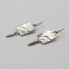 Left facing hammered silver rectangle earrings on gray surface Silver Hammered Sterling Silver Linear Earrings, Modern Sterling Silver Hammered Linear Earrings, Modern Sterling Silver Linear Earrings With Hammered Detail, Modern Hammered Sterling Silver Linear Earrings, Hammered Sterling Silver Long Drop Earrings, Modern Sterling Silver Hammered Earrings, Modern Hammered Sterling Silver Earrings, Contemporary Hammered Silver Jewelry, Contemporary Hammered Sterling Silver Earrings