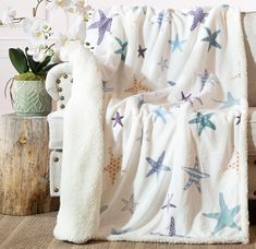 a blanket with starfishs on it next to a chair and flowers in a vase