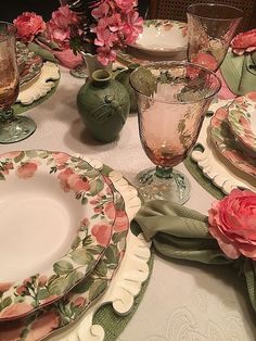 the table is set with pink flowers and green china plates, napkins, and vases