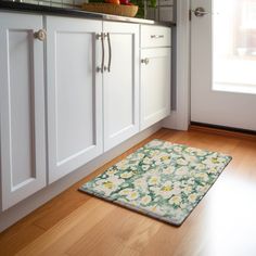 a kitchen with white cabinets and wood flooring next to a door way that leads to the outside