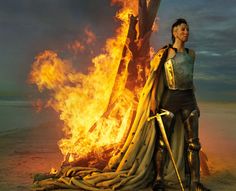 a woman in armor standing next to a pile of fire retardants on the beach