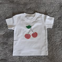 a white t - shirt with two cherries on it sitting on the floor next to a carpet