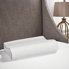 a white pillow sitting on top of a bed next to a lamp