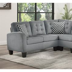 a gray sectional couch with pillows on it in front of a large window and rug