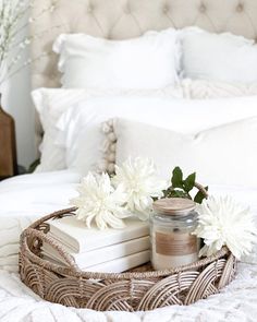 a basket with books and flowers sitting on top of a bed next to a candle