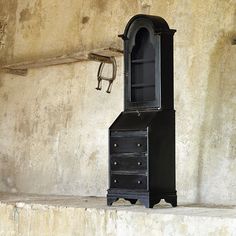 an old black grandfather clock sitting on top of a stone step next to a wall