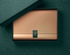 a green and gold box with a flower on the front is sitting on a dark green surface