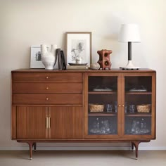 a wooden cabinet with glass doors and two vases on top, next to a lamp