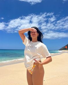 a woman standing on top of a sandy beach next to the ocean with her hands behind her head