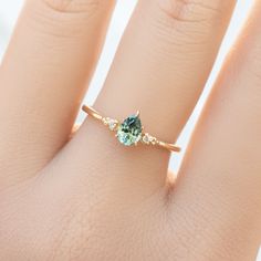 a woman's hand with a gold ring and two green stones on the band