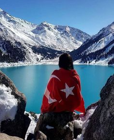 a man sitting on top of a rock next to a large lake covered in snow