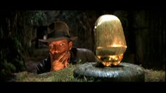 a man wearing a hat next to a golden statue in the woods with eyes drawn on it