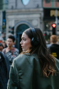 a woman with headphones on walking down the street in front of some people and buildings