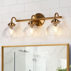 a bathroom vanity with three lights and a mirror on the wall next to it in front of a white tiled wall