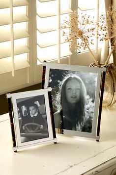 two frames sitting on top of a table next to a vase with flowers in it