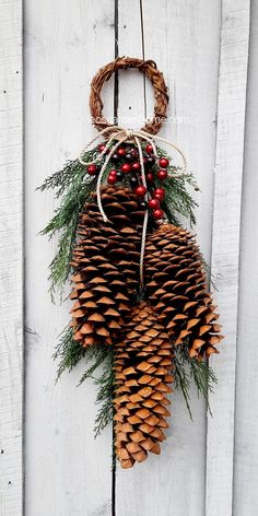 a pine cone hanging on a white wooden wall with berries and greenery attached to it