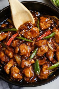 a skillet filled with chicken and vegetables on top of a white table cloth next to a wooden spoon