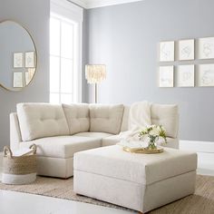 a living room with a white sectional couch and ottoman in it's center area