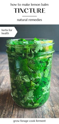 a glass jar filled with green leaves on top of a wooden table next to text that reads how to make lemon balm tincture natural remedies