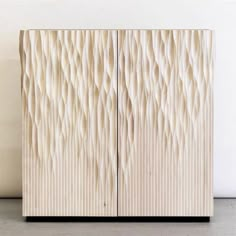 a wooden cabinet sitting on top of a floor next to a white wall with wavy lines