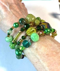 This green beaded bracelet wraps 4 times around the wrist.  It features a hand painted bead, two vintage wooden beads dating from a 1950s necklace, two olive green plastic beads from a 60's necklace, czech crystal beads in several shades of green, unique glass beads and some small vintage pearls.  It will match any green clothes you have because every hue of green possible is represented.  It is bling in a subtle way! Green Oval Beads Bracelet As A Gift, Green Multi-strand Jewelry For Gift, Spiritual Green Beaded Bracelets With Faceted Beads, Green Wooden Beaded Bracelets As Gift, Green Adjustable Beaded Bracelets With Oval Beads, Adjustable Green Beaded Bracelets With Wooden Beads, Handmade Green Beaded Bracelets With Oval Beads, Adjustable Green Beaded Bracelet, Adjustable Green Beaded Bracelets