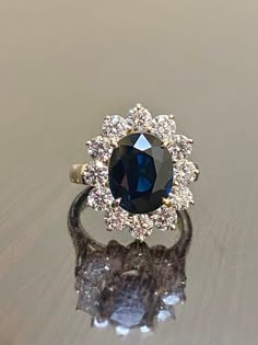 DeKara Designs Clearance Metal- 14K Yellow Gold, .583. Stones- Genuine Australian Oval Blue Sapphire 3.60-3.80 Carats, 12 Round Diamonds H-I Color SI1 Clarity, 1.50 Carats. Size- 3-12 Handmade 14K Yellow Gold Sapphire and Diamond Ring. This ring is inspired by Princess Diana and the Art Deco era with an enticing Australian fiery oval shaped midnight blue sapphire. The sapphire is professionally set in between four prongs. The sapphire has a halo of prong set 12 round diamonds surrounding them wh Sapphire Cluster Diamond Ring For Wedding, Timeless Blue Sapphire Wedding Ring, Elegant Blue Cluster Diamond Ring, Wedding White Gold Cluster Sapphire Ring, Cluster Sapphire Wedding Ring, Cluster Sapphire Ring With Center Stone For Wedding, Wedding Sapphire Cluster Ring In White Gold, Blue Cluster Sapphire Ring For Wedding, Blue Diamond Halo Ring For Wedding