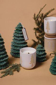 three candles are sitting next to small trees and pinecone cones on a brown background