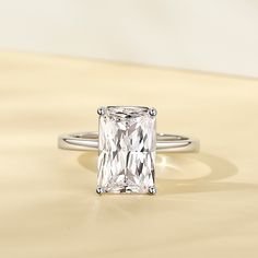 an engagement ring with a square cut diamond in the center on a beige surface,