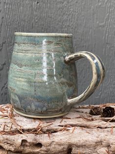 a green mug sitting on top of a piece of driftwood next to a gray wall