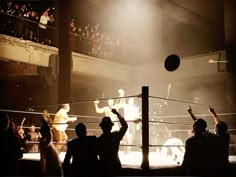 two men are playing with a ball in the middle of a boxing ring while people watch