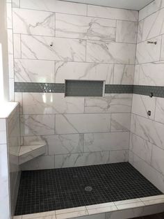 a bathroom with white marble walls and floor tiles on the shower wall, along with a black tiled floor