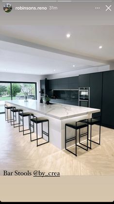 an image of a modern kitchen setting with bar stools in the foreground and large windows on the far wall