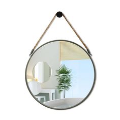 a round mirror hanging on a rope in front of a white room with a potted plant